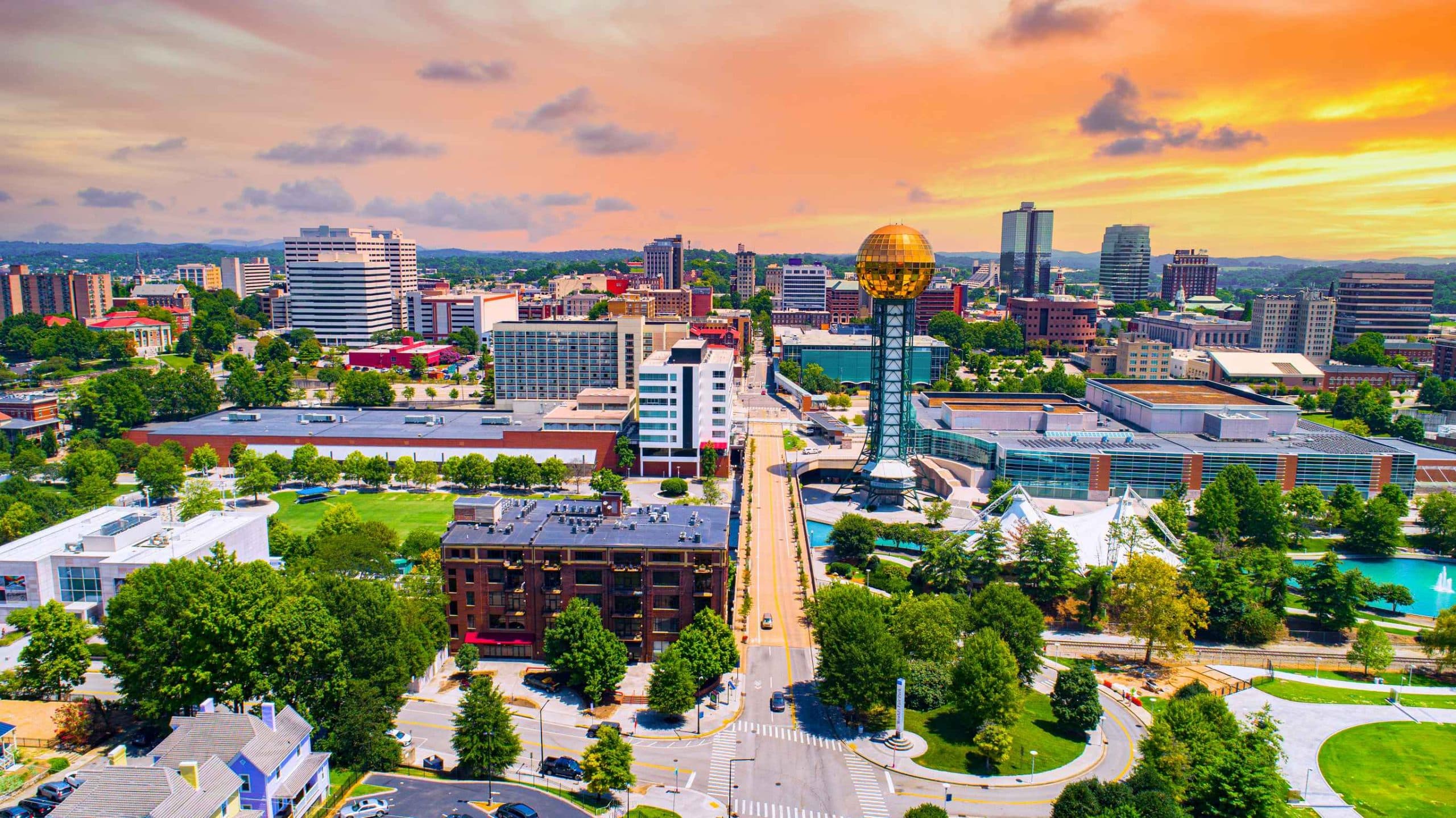 Aerial view of a modern downtown business district at golden hour with sleek glass office towers and warm light reflecting across the cityscape